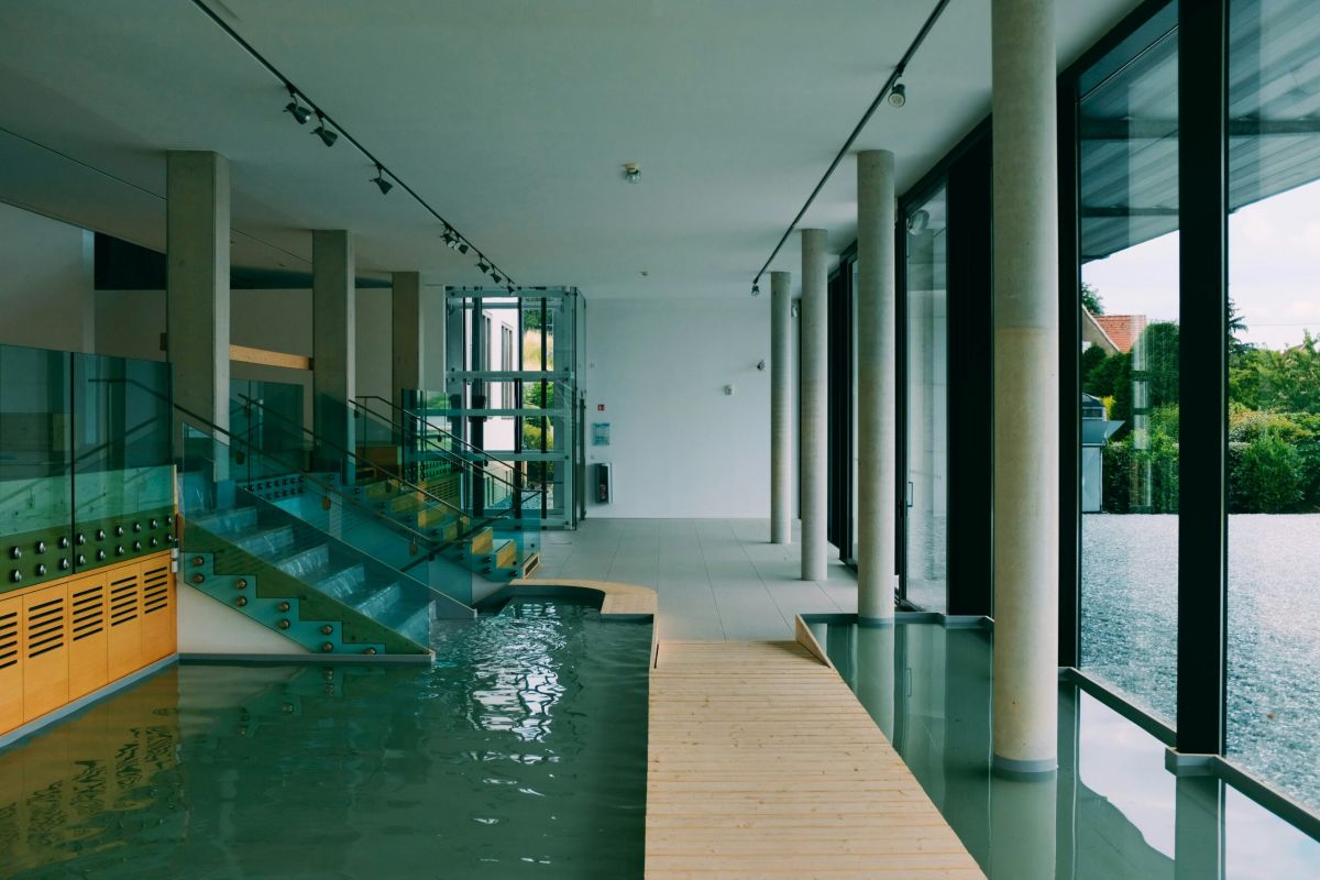 Modern apartment complex with a pool, lounge chairs, palm trees, and three-story buildings in the background.