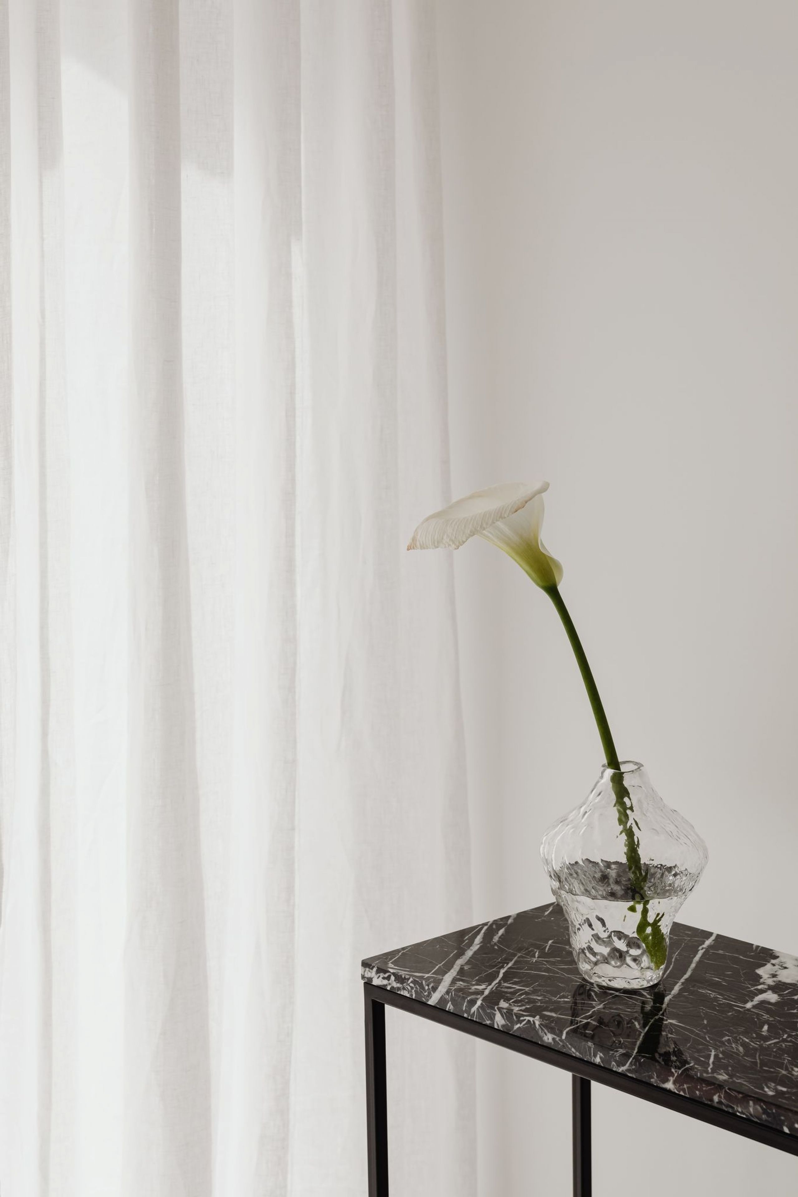 Glass vase on black marble table with cut orchid and white curtain